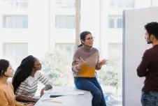 Four college students having a discussion in front of a window; one is talking and the others are listening